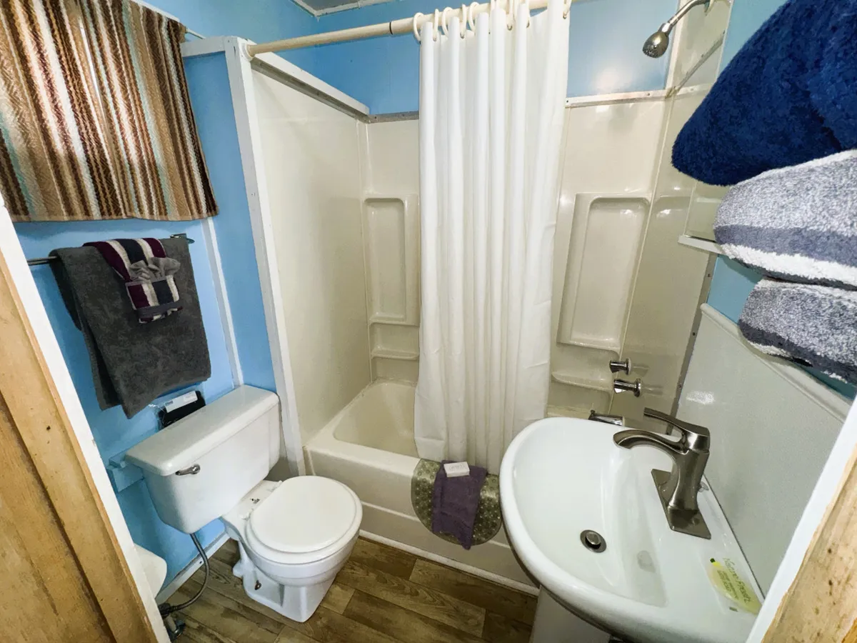 A well-appointed ensuite bathroom featuring a shower with a curtain, a vanity sink, toilet, and fresh towels. The space is clean and functional, providing a private sanctuary for unwinding and self-care.