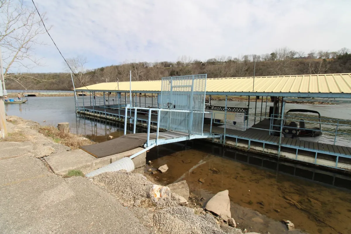 A peaceful lakeside setting with a boat dock stretching into calm water, framed by surrounding hills and gentle reflections on the water’s surface. The tranquil mood invites thoughts of fishing, relaxing, or enjoying nature at sunset.