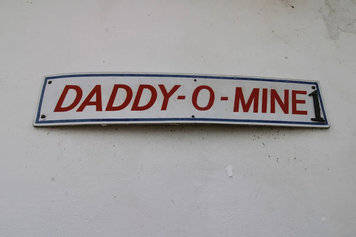 A cozy inside scene featuring a wall sign that reads 'DADDY-O-MINE,' with warm lighting and hints of a lived-in, welcoming atmosphere. Though less specific to the kitchen, it conveys the warmth and social aspect of gathering indoors.